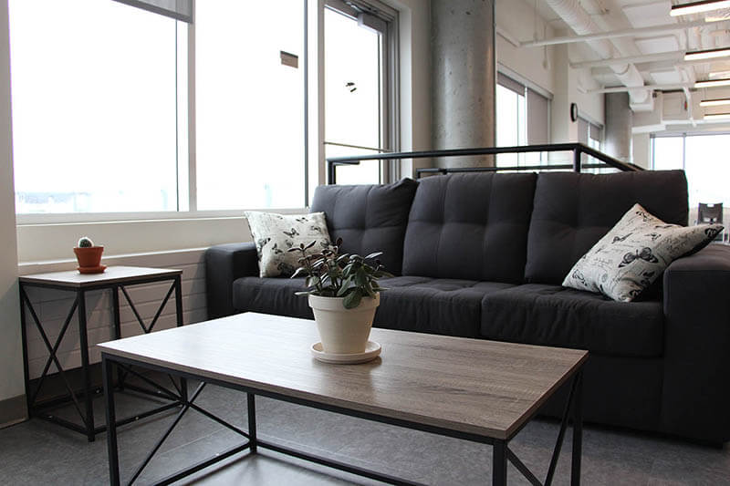 Espace de détente pour lire ou discuter entre collègues avec un sofa, des coussins, deux tables basses et des plantes d’intérieur.